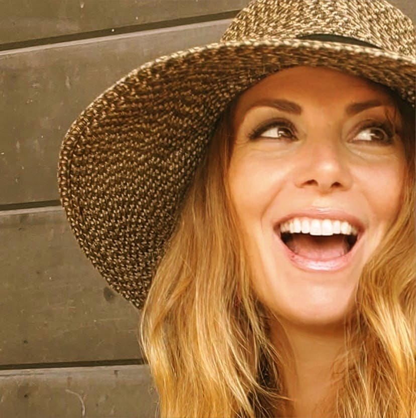 Kerry Ingram, founder of Held by the Village, laughing in a straw hat